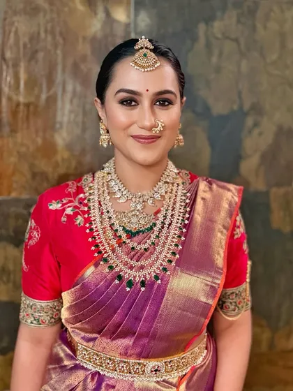 A vibrant and joyful look featuring kohl-defined eyes and glowing skin. The makeup is designed to harmonize with the rich jewel tones of her saree and the intricate diamond and emerald jewellery, creating a look of divine grace.