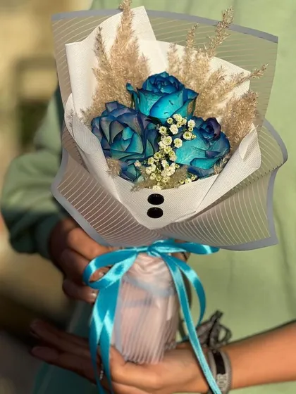 A unique bouquet of dyed blue roses, perfect for someone who loves unconventional beauty. The roses are accented with dried pampas grass and wrapped in a stylish white paper with a blue ribbon.