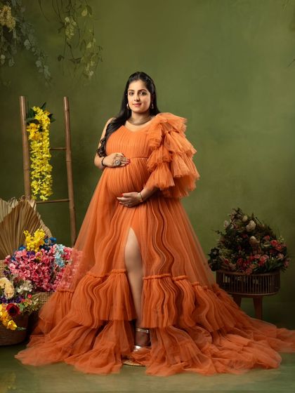 A vibrant portrait of a mom-to-be in a stunning orange ruffled gown, surrounded by colorful flowers in the studio.