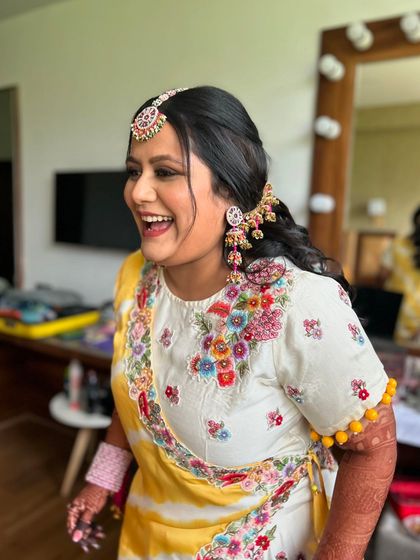 A happy Haldi bride with her hair in a half-up style, adorned with a colorful, traditional accessory.
