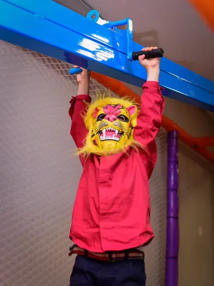 Roaring into fun! A child in a lion mask hangs from the play structure, fully in character.