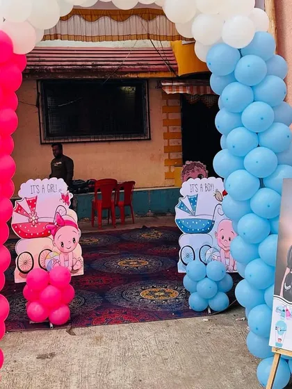 The entrance to a baby shower, featuring a pink and blue balloon arch and a personalized welcome sign with the parents' photo.
