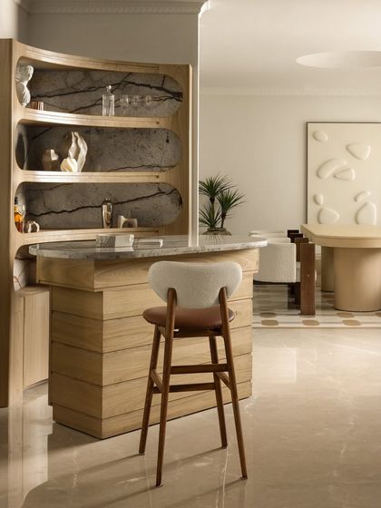 The bar is the centerpiece of Ecru Maison, crafted in warm light wood with a polished marble countertop. We designed the organically curved shelves against a dramatic marble backdrop to be both a functional hub and a sculptural feature.