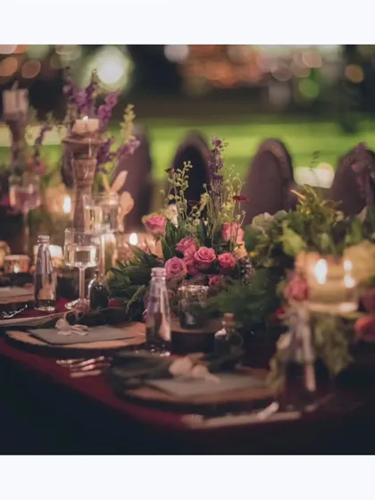 A close-up of a rustic yet elegant tablescape. The deep colors, lush floral arrangements, and candlelight create a warm and inviting mood for an evening dinner party.
