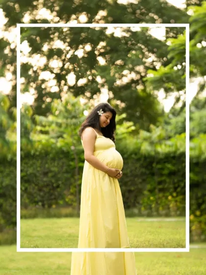 A beautiful solo portrait in a sun-drenched park. The mother-to-be in a bright yellow dress looks serene as she holds her baby bump.