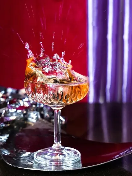 A celebratory splash in a coupe glass, set against a festive red and silver background. This dynamic shot is perfect for New Year's Eve or any party-themed promotion.