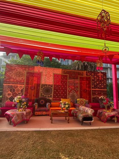 A wide view of a seating area at the Kathiyawadi Haldi, showing the vibrant mix of colors in the ceiling drapes and the rich textures of the textile backdrop.