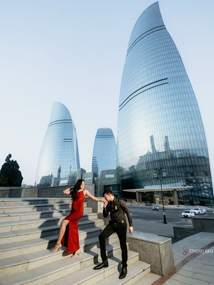 A chivalrous moment captured on the steps in front of Baku's Flame Towers. The low angle emphasizes the grandeur of the architecture and the elegance of the couple's interaction.