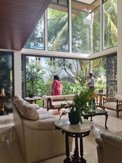 This image captures the double-height living space of our "Mango Tree" house, where the architecture is built around the natural landscape. The expansive glass walls invite the garden inside, creating a serene and light-filled environment.