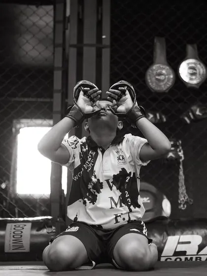 A young fighter kneels inside the cage, a moment of quiet focus before the storm. This black and white shot captures his determination.