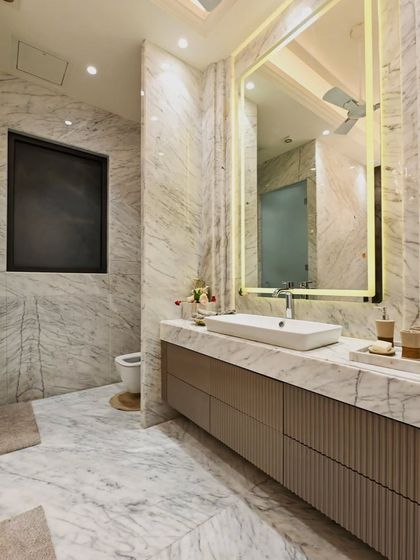 This bathroom is a spotlight on elegance and modern comfort. The all marble design, from walls to floor, is complemented by a floating vanity with reeded drawer fronts and a large, backlit mirror.