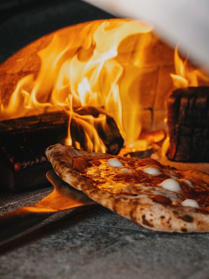 I am busy in the kitchen, prepping delicious pizzas to serve you the best. A Margherita pizza bakes in the intense heat of the wood-fired oven.