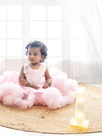 A beautiful portrait of the birthday girl in her fluffy pink dress, ready for her cake smash. The natural light from the window creates a soft, dreamy look.