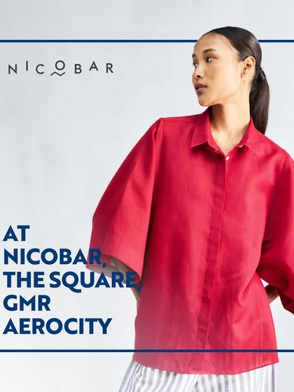 A model wearing a bold red shirt from Nicobar, demonstrating their use of vibrant color within their minimalist design ethos.