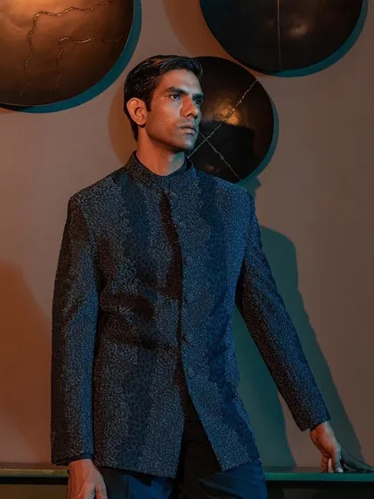 A profile view of a textured blue Bandhgala jacket. The lighting catches the intricate weave of the fabric, showcasing the quality and attention to detail that goes into every bespoke piece.