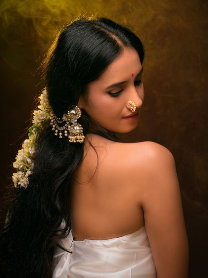 A classic ethnic portrait with a focus on traditional jewelry. The warm lighting and rich brown background create a painterly effect, emphasizing the model's serene beauty.