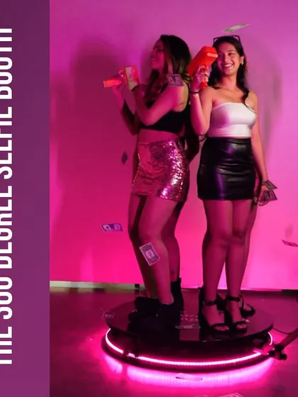 Two guests having a blast on the 360 Degree Selfie Booth platform, complete with fun props like money guns. We provide a variety of props to elevate the video experience.
