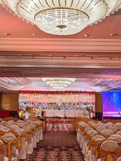 A wide-angle view of the grand wedding hall, showing the opulent stage and the beautifully arranged seating. The entire space is unified by the red and gold theme, creating a cohesive and luxurious atmosphere.