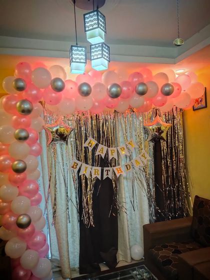 A beautiful pink, white, and silver balloon arch for a home birthday celebration. The arch is set against a silver tinsel curtain.
