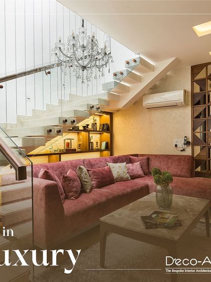Live in luxury with this duplex living area design. A dramatic floating staircase and a crystal chandelier create a stunning focal point, complemented by a plush rose-colored sectional sofa for ultimate comfort.