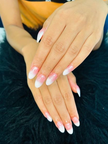 A soft ombre effect on long, pointed nails, blending from a natural pink base to a milky white tip.