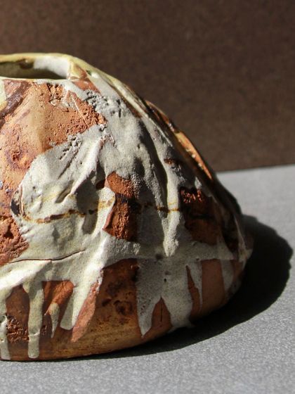 A close up of a round Kurinuki vase, showing the dripping effect of the glaze over its textured, carved surface.