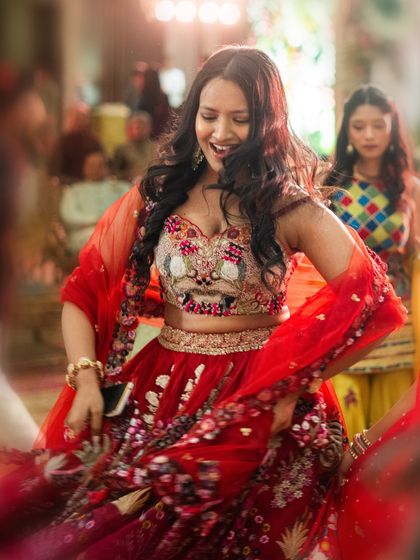 A bridesmaid twirls on the dance floor in a stunning red floral lehenga. We ensure that every member of the bride's tribe has an outfit that they love and feel amazing in.