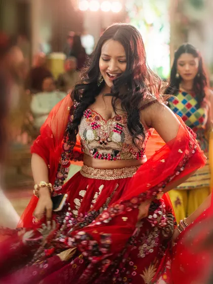 A bridesmaid twirls on the dance floor in a stunning red floral lehenga. We ensure that every member of the bride's tribe has an outfit that they love and feel amazing in.
