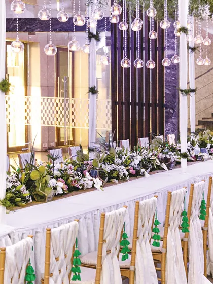 An elegant reception table setup featuring classic white roses, lilies, and green tassels. The clean and timeless aesthetic provides a beautiful canvas for a memorable wedding dinner.