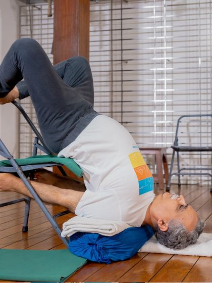 A student practices a supported inversion using a chair and bolster. This restorative pose is excellent for calming the nervous system, relieving fatigue, and reducing swelling in the legs.