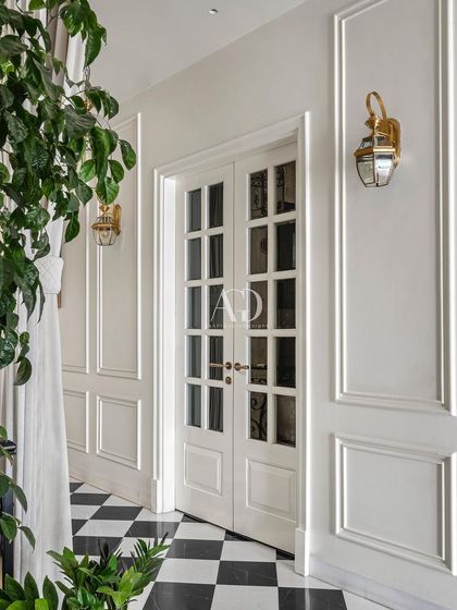 Detail of a French door and paneled wall, demonstrating how I use millwork to add texture and architectural interest. The classic checkerboard floor and warm glow from the wall sconce contribute to a welcoming and sophisticated entryway.