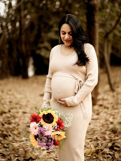 A lovely portrait of the mom-to-be in the woods, holding a vibrant bouquet of flowers and looking down at her bump with a gentle smile.