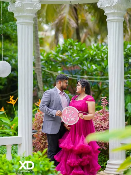 A sweet gender reveal moment, with the couple holding an "It's a girl" sign in a beautiful garden setting.
