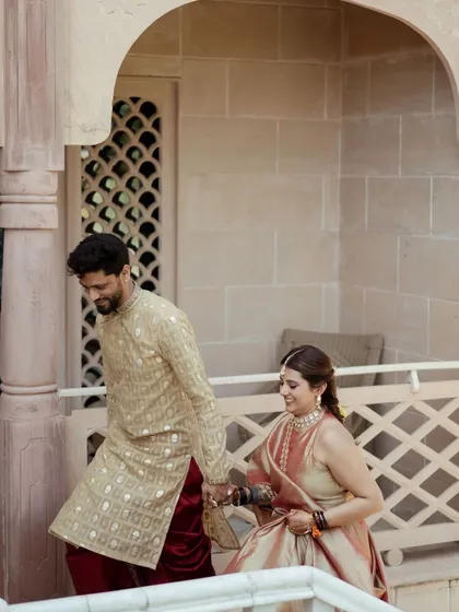 A candid moment of the couple walking hand-in-hand through the corridors of the palace venue. Their traditional outfits and the beautiful architecture create a royal feel.