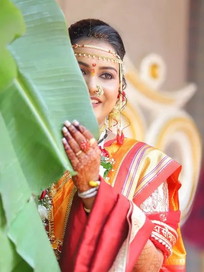 A playful and creative shot of the bride peeking from behind a banana leaf. It's a unique take on a traditional portrait, showcasing her fun personality.