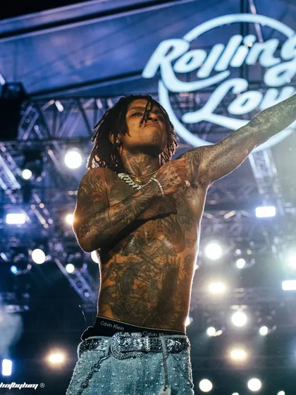 Swae Lee owns the stage at Rolling Loud India, shirtless and pointing to the crowd. This wide shot captures his full stage presence against the massive festival branding, showcasing the scale of the event.