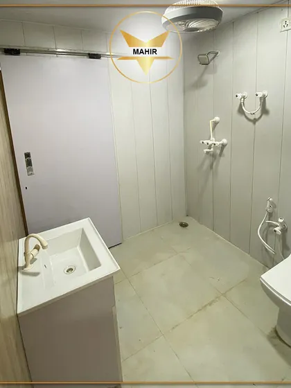 A clean and modern bathroom inside our portable living unit. It is equipped with a toilet, a space-saving vanity with a sink, a handheld shower, and a bidet sprayer, ensuring all the comforts of a traditional home.