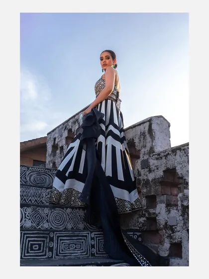 A powerful low-angle shot of a model on a decorated staircase, wearing a modern black and white lehenga. This perspective accentuates the dramatic flow of the skirt and creates a strong, statuesque silhouette.
