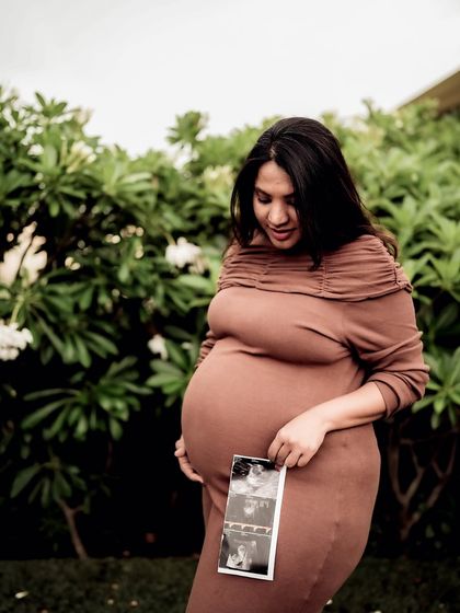 A serene portrait of the mom-to-be in a garden, looking down at the sonogram pictures held against her bump.