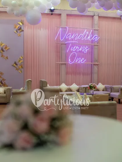 A quiet corner of the party, featuring the custom neon sign "Nandika Turns One." The soft lighting and elegant seating create a serene and beautiful atmosphere.