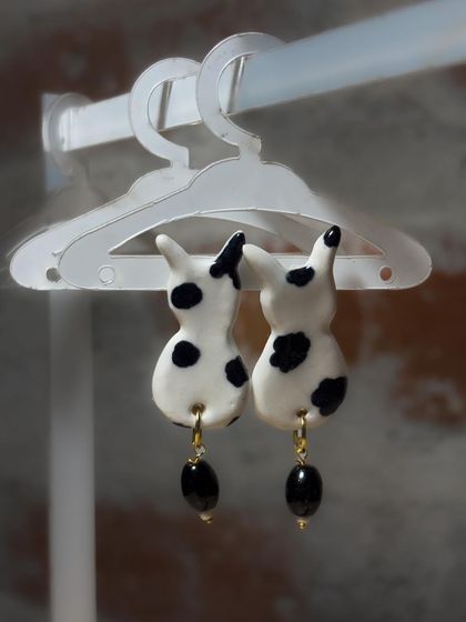 A pair of handmade ceramic earrings shaped like spotted bunnies, complete with black bead drops. This is an example of the wearable art from my 'Paw-try' collection.