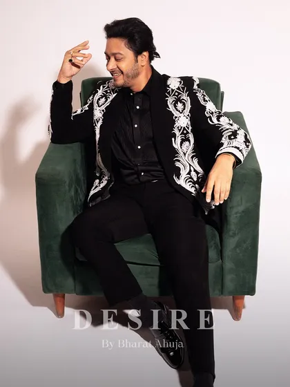 A relaxed yet powerful pose in the black embroidered blazer. The intricate white detailing on the sleeves and lapels stands out against the dark fabric, showcasing true craftsmanship.