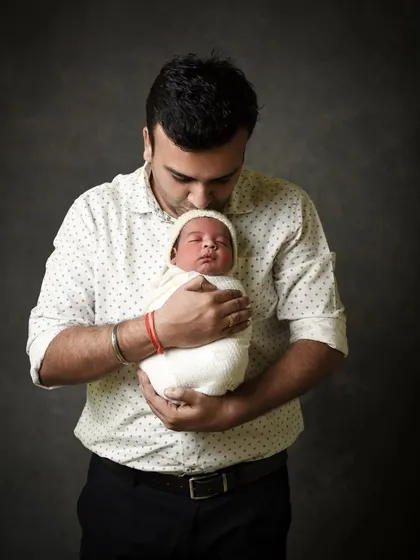 A classic father and newborn portrait. The father's gentle hold and loving kiss convey a sense of warmth and protection. The simple, dark background keeps the focus on this beautiful bond.