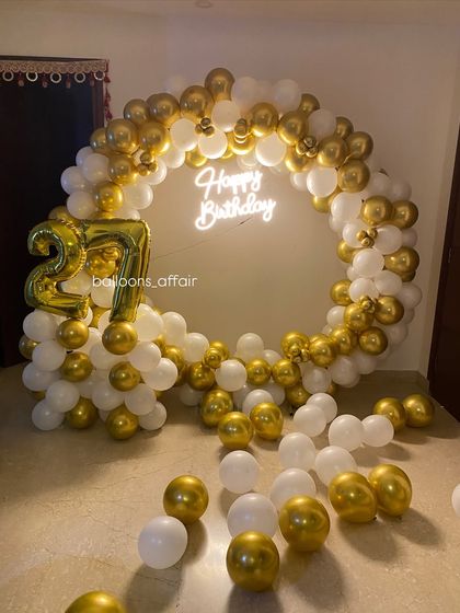 This photo shows the full circular balloon backdrop for a 27th birthday, with a 'Happy Birthday' neon sign glowing in the center.