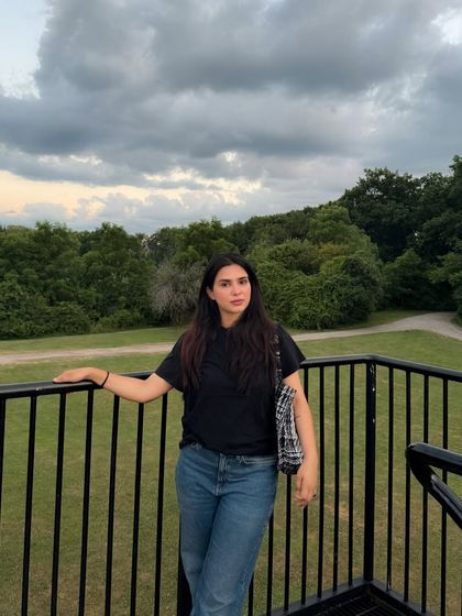 Posing on a lookout, this image shows a casual outfit against a backdrop of lush greenery.