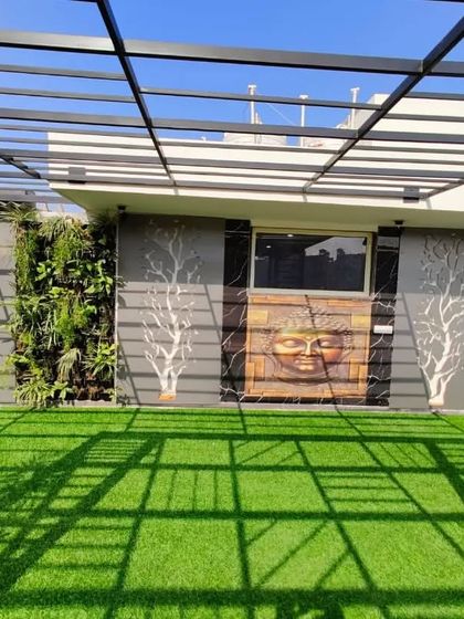 A frontal view of the feature wall, with the Buddha art centered between two vertical gardens and two backlit tree sculptures, under a modern pergola.