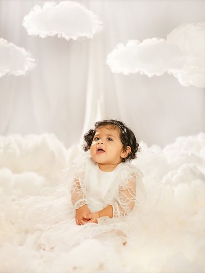 A quiet, contemplative moment for the birthday girl, sitting peacefully in her cloud-themed studio setup. The all-white aesthetic is so dreamy.