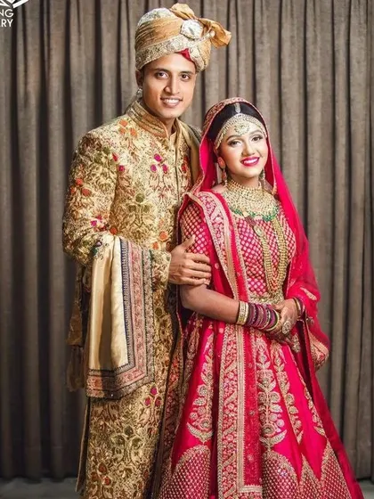 Make a statement with vibrant colors. This couple is coordinated in a striking combination of fuchsia pink and gold. The bride's heavily embroidered pink lehenga and the groom's floral embroidered gold sherwani create a picture-perfect look for a sangeet or wedding day.