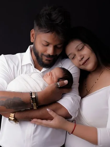 A wider shot of the family admiring their newborn. This image captures the serene and loving atmosphere of the studio session, highlighting the family's first moments together.