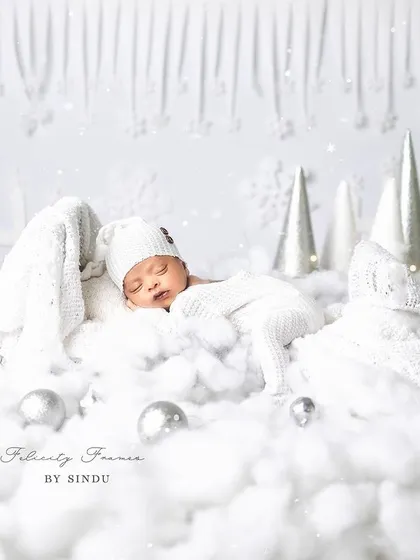 A perfect little snowflake dreaming in a winter wonderland. This all-white setup with soft cotton clouds and twinkling lights creates a magical, serene atmosphere for a newborn photoshoot.
